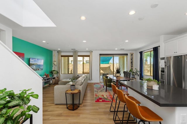 kitchen featuring a breakfast bar area, light hardwood / wood-style flooring, white cabinets, and stainless steel refrigerator with ice dispenser