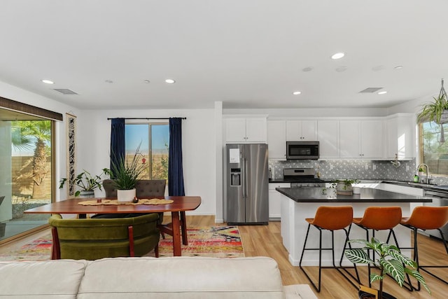 kitchen featuring stainless steel appliances, white cabinets, backsplash, a kitchen island, and light wood-type flooring