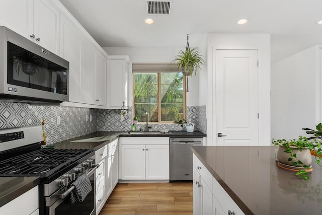 kitchen with white cabinets, sink, light wood-type flooring, appliances with stainless steel finishes, and tasteful backsplash