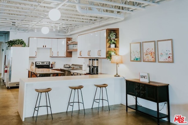 kitchen featuring a kitchen breakfast bar, kitchen peninsula, white cabinets, and concrete flooring