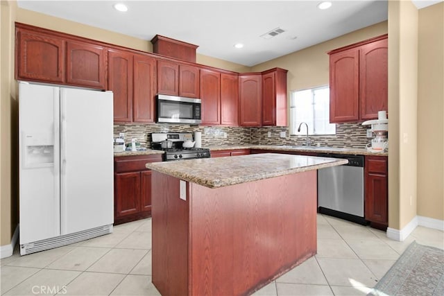 kitchen with appliances with stainless steel finishes, backsplash, a kitchen island, and light tile patterned flooring