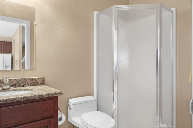 bathroom featuring a shower with door, vanity, and toilet