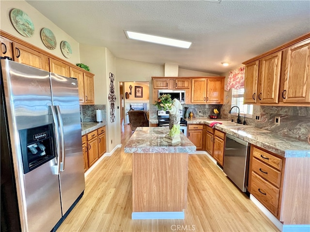 kitchen with lofted ceiling, stainless steel appliances, sink, a center island, and light wood-type flooring