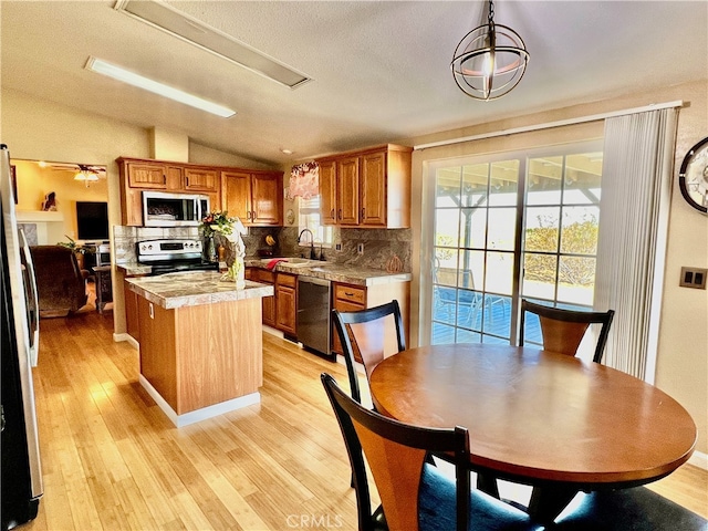 kitchen with lofted ceiling, a kitchen island, light wood-type flooring, pendant lighting, and stainless steel appliances