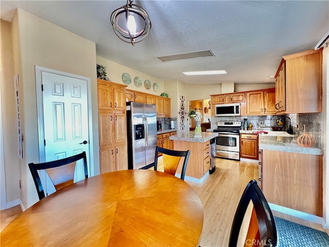 kitchen with lofted ceiling, a kitchen island, appliances with stainless steel finishes, light hardwood / wood-style floors, and tasteful backsplash