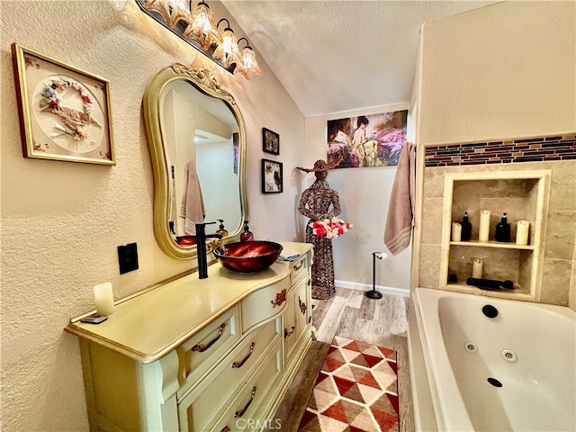 bathroom featuring wood-type flooring, a tub, a textured ceiling, vaulted ceiling, and vanity