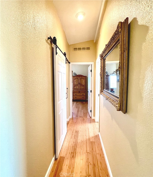 hall featuring lofted ceiling, a barn door, and hardwood / wood-style flooring