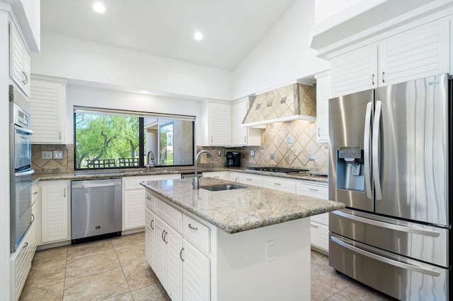 kitchen featuring appliances with stainless steel finishes, custom range hood, a center island with sink, white cabinetry, and lofted ceiling