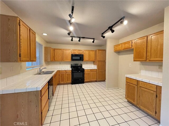 kitchen with tile counters, black appliances, track lighting, and sink