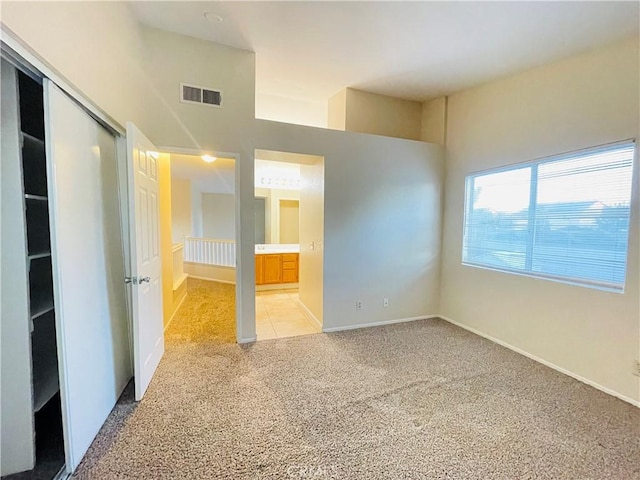 unfurnished bedroom with light carpet, ensuite bathroom, and a closet