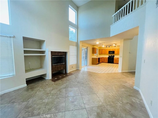 unfurnished living room with light tile patterned flooring, a towering ceiling, and built in features