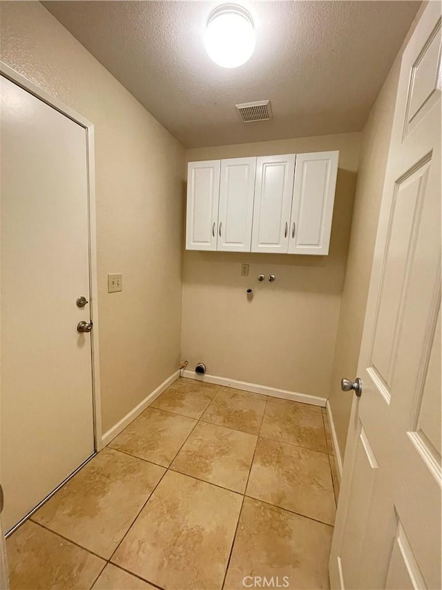 clothes washing area featuring washer hookup, cabinets, light tile patterned floors, and a textured ceiling