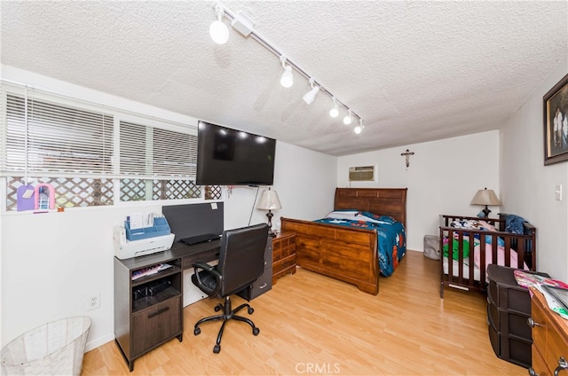 bedroom featuring track lighting, a wall unit AC, a textured ceiling, and light hardwood / wood-style floors