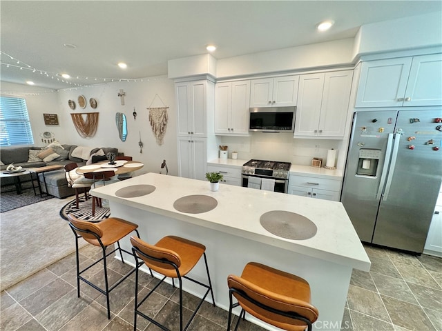 kitchen featuring white cabinets, stainless steel appliances, light colored carpet, and a kitchen breakfast bar