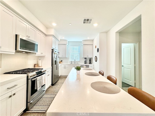 kitchen featuring appliances with stainless steel finishes, white cabinetry, light stone countertops, a kitchen bar, and sink