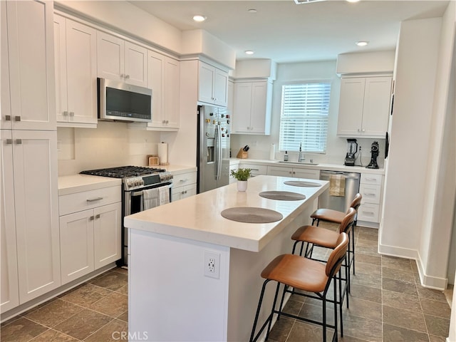 kitchen with stainless steel appliances, sink, a center island, a breakfast bar, and white cabinetry