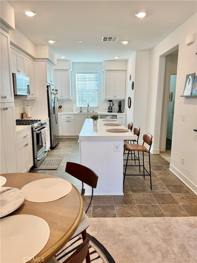 kitchen featuring sink, a center island, a kitchen breakfast bar, white cabinetry, and stainless steel appliances