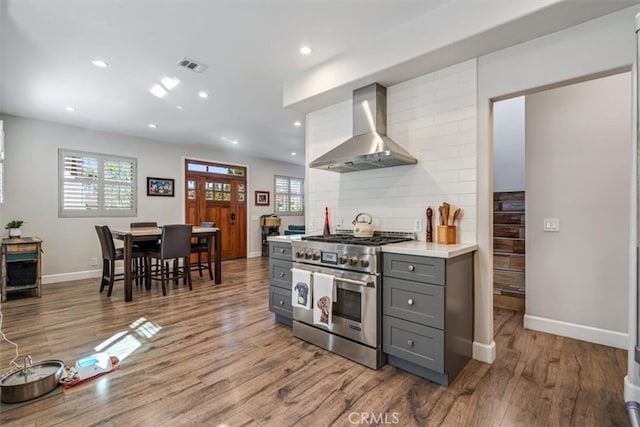 kitchen featuring high end range, decorative backsplash, light hardwood / wood-style flooring, gray cabinetry, and wall chimney exhaust hood