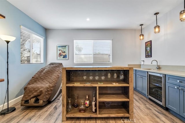 bar featuring beverage cooler, decorative light fixtures, sink, light hardwood / wood-style flooring, and blue cabinets