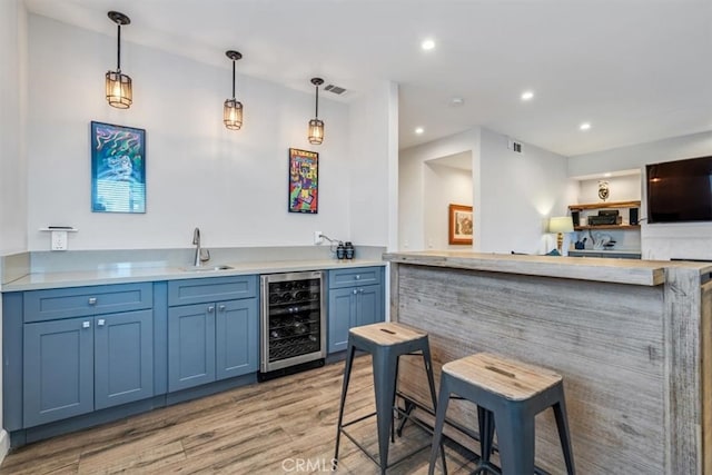 bar with wine cooler, light hardwood / wood-style flooring, blue cabinets, and pendant lighting