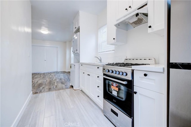 kitchen featuring under cabinet range hood, light countertops, range with gas stovetop, stainless steel refrigerator, and white cabinets