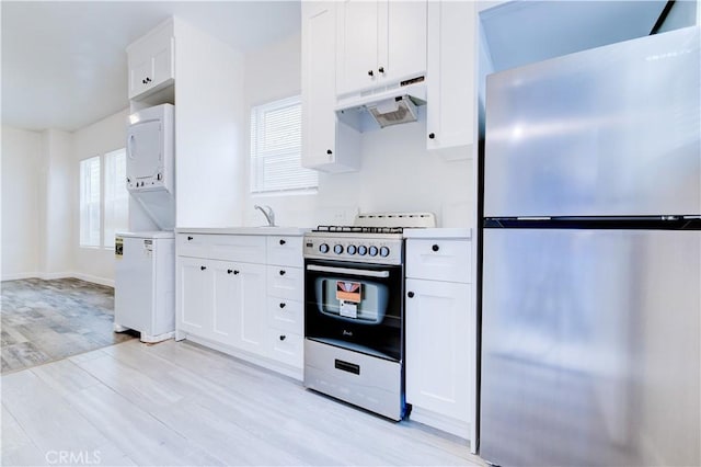 kitchen with stacked washer / drying machine, light hardwood / wood-style flooring, stainless steel fridge, stove, and white cabinets