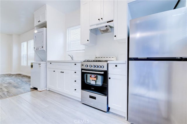 kitchen featuring gas stove, freestanding refrigerator, light wood-style floors, under cabinet range hood, and stacked washer / dryer