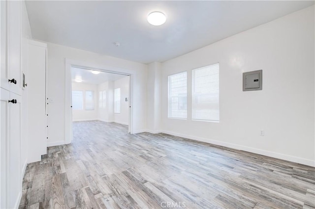 unfurnished room with electric panel, baseboards, and light wood-style floors