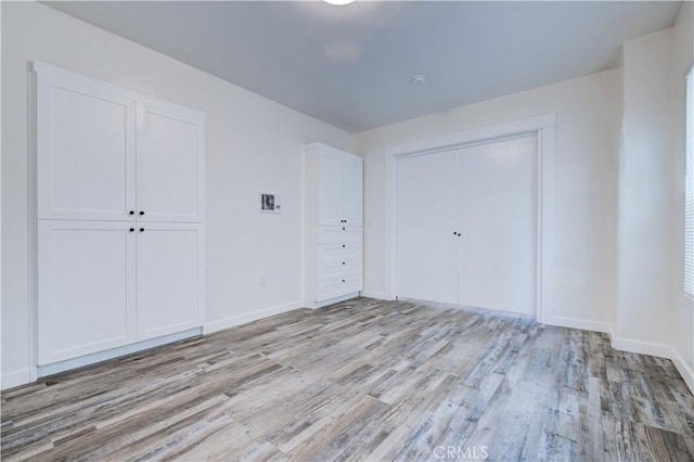 unfurnished bedroom featuring a closet, light wood-style flooring, and baseboards