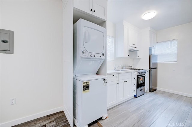 clothes washing area with a sink, light wood-type flooring, baseboards, and stacked washer and dryer