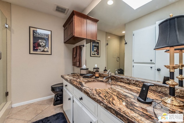 bathroom featuring tile patterned flooring, vanity, walk in shower, and a skylight