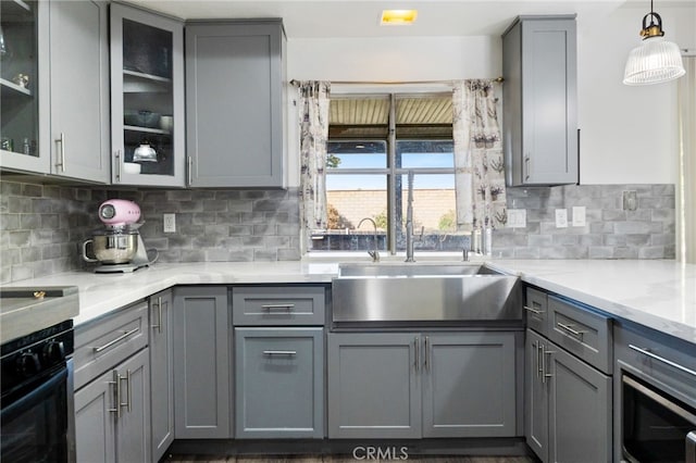 kitchen featuring gray cabinetry, light stone countertops, sink, oven, and decorative backsplash