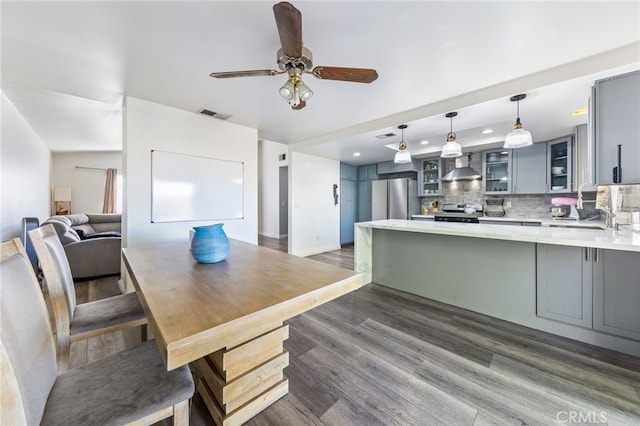 kitchen with wall chimney range hood, kitchen peninsula, tasteful backsplash, appliances with stainless steel finishes, and gray cabinetry