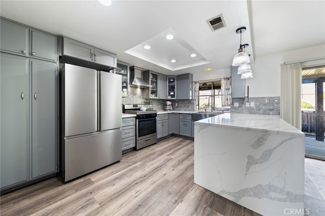 kitchen with appliances with stainless steel finishes, a healthy amount of sunlight, hanging light fixtures, and wall chimney range hood