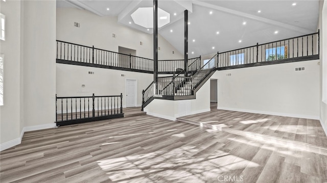 interior space featuring beamed ceiling, a skylight, high vaulted ceiling, and light wood-type flooring