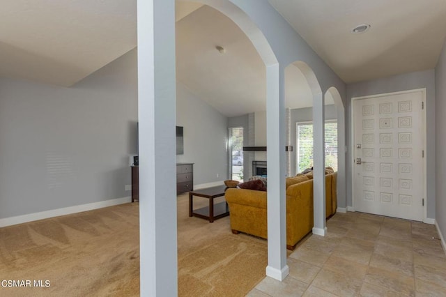 carpeted entryway with a large fireplace and vaulted ceiling