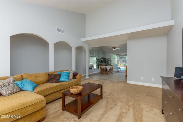 carpeted living room with ceiling fan and a high ceiling