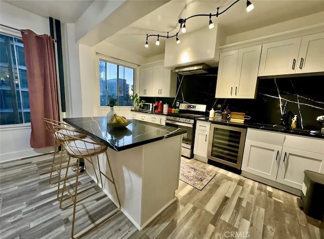 kitchen featuring stainless steel range, white cabinetry, wine cooler, and tasteful backsplash