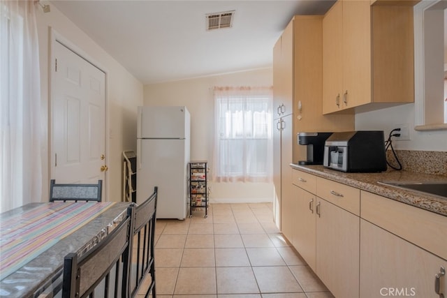 kitchen featuring white fridge, light tile patterned flooring, lofted ceiling, and light brown cabinetry