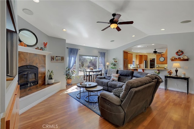 living room with a tile fireplace, vaulted ceiling, light hardwood / wood-style floors, and ceiling fan