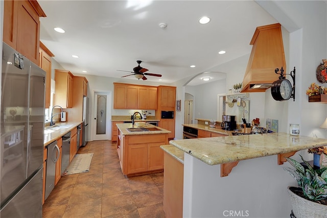 kitchen featuring kitchen peninsula, light stone counters, custom range hood, sink, and stainless steel appliances