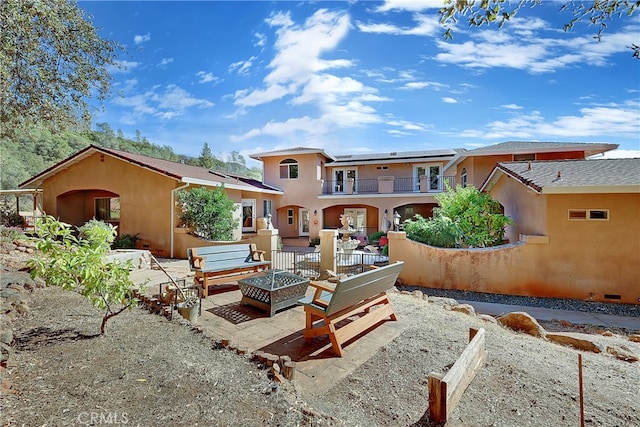 rear view of house with a balcony, a patio, and a fire pit