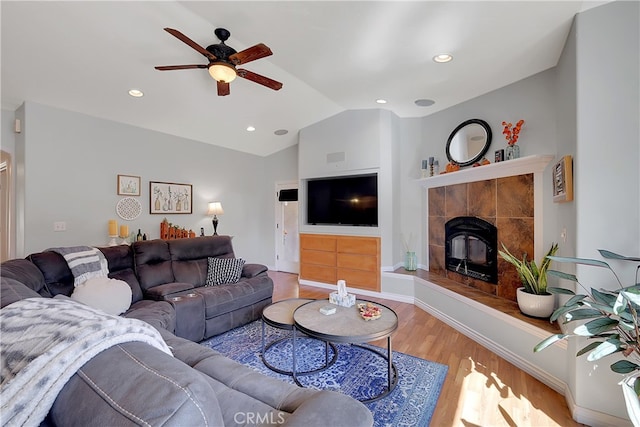 living room featuring a tiled fireplace, hardwood / wood-style flooring, lofted ceiling, and ceiling fan