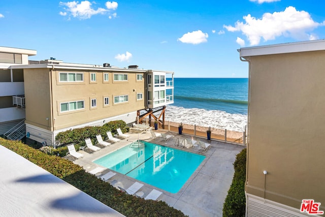 view of swimming pool with a water view, a patio area, and a view of the beach