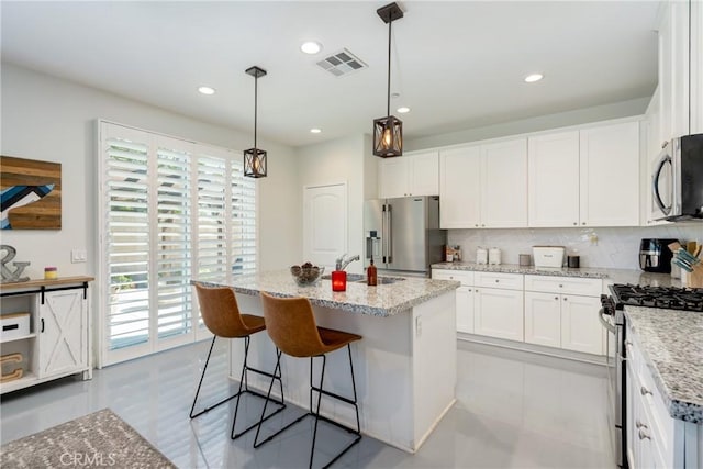 kitchen with stainless steel appliances, pendant lighting, white cabinetry, and an island with sink