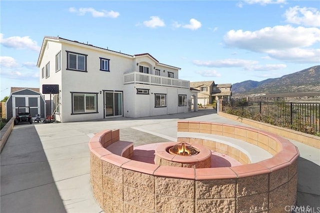 rear view of property featuring an outdoor fire pit, a mountain view, a balcony, a shed, and a patio area