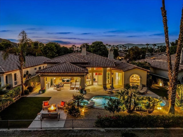 back house at dusk with an outdoor living space with a fire pit, a pool with hot tub, and a patio