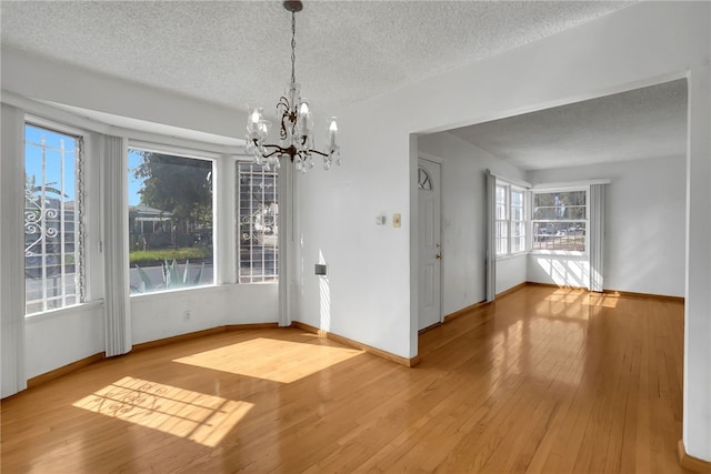 unfurnished dining area featuring hardwood / wood-style flooring, a textured ceiling, and a chandelier