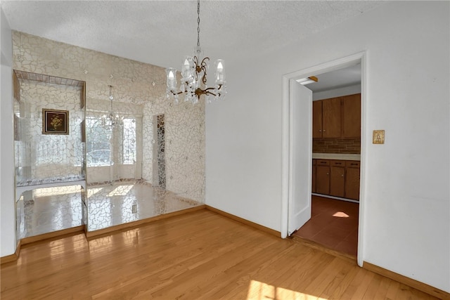 unfurnished dining area with wood-type flooring, a textured ceiling, and a notable chandelier