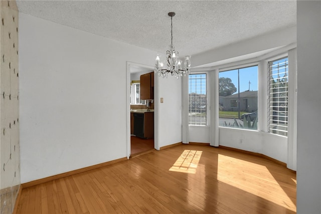 unfurnished dining area with a chandelier, a textured ceiling, and light wood-type flooring